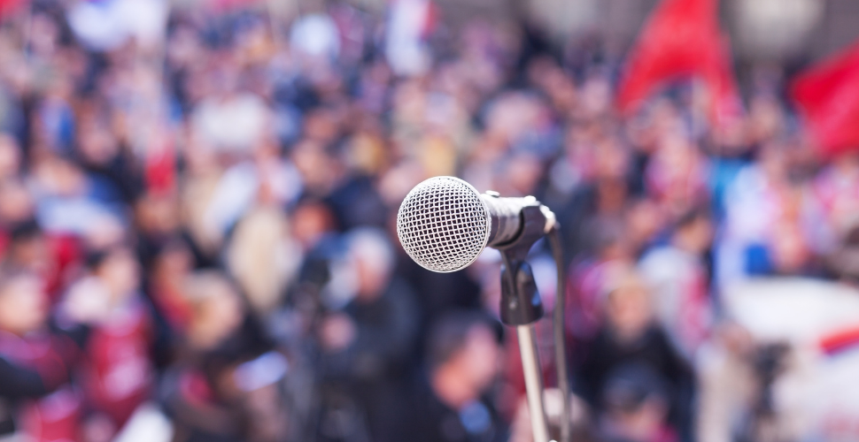 A microphone in focus with a blurred crowd in the background, symbolising youth engagement, activism, and the importance of giving young people a platform to be heard.