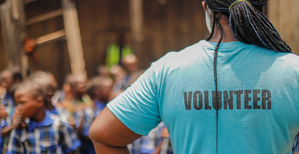 A volunteer wearing a turquoise shirt stands in front of a group of children, symbolising the vital role of people and leadership within the third sector.