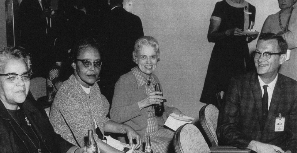 Historic black and white photo showing women seated and smiling at a gathering, representing pioneers Katherine Johnson, Dorothy Vaughan, and Mary Jackson whose work transformed science and space exploration.