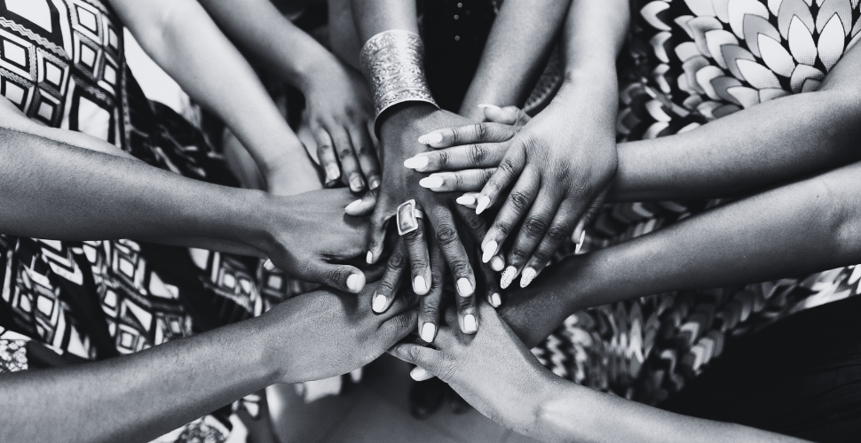 Black and white image showing a circle of women’s hands joined together, symbolising unity, strength and the celebration of Black women’s contributions.