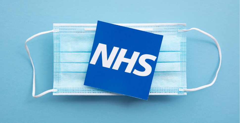 A blue NHS card placed on top of a disposable face mask, representing healthcare resilience and recovery after the pandemic.