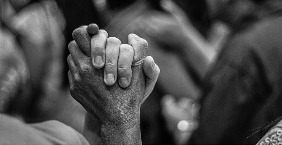 Close-up black and white photo of two people holding hands tightly, symbolising unity, allyship, and collective strength against racism.