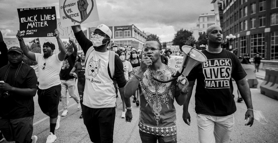 A group of protestors march together holding Black Lives Matter signs and a megaphone, symbolising unity and the fight against racial injustice.